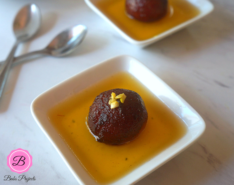Individual Servings of Gulab Jamun on White Dishes and Spoons on the Side