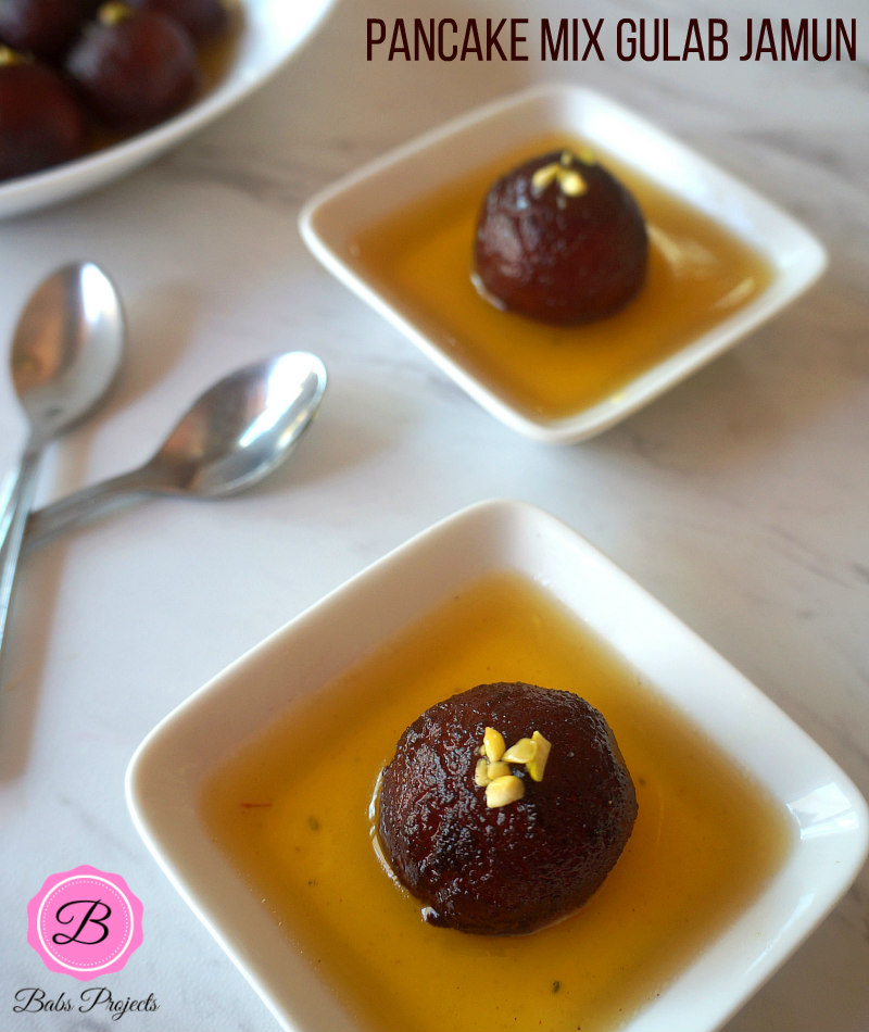 Single Servings of Gulab Jamun with Sugar Syrup on White Dishes and Spoons on the Side.