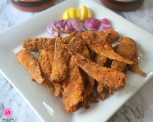 Crispy Fried Mandeli Fish on a White Platter with Onions and Lemons Slices on the Side