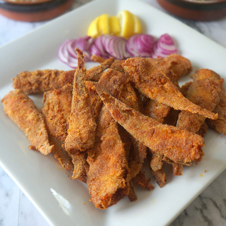 Crispy Fried Mandeli Fish on a White Platter with Onions and Lemons Slices on the Side